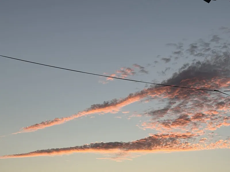Two clouds are backlit in orange against a blue grey sky. They form a sharp angle, a lone power line bisects the frame.